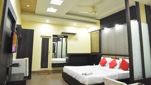 Quarto de hotel com cama, ventilador de teto, ar condicionado, televisão e espelho.