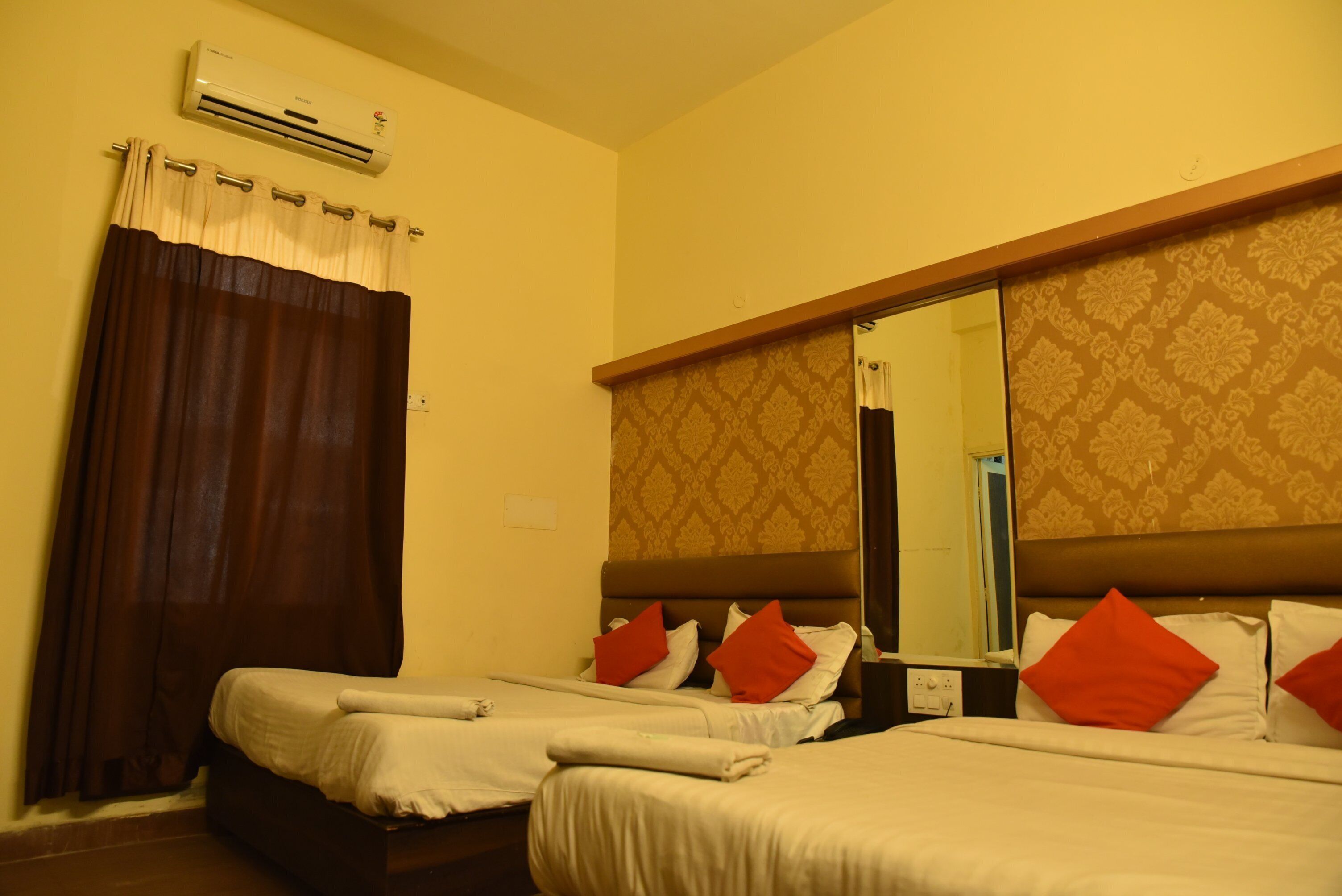 A hotel room with two beds, a large mirror, an air conditioner, and a curtain.