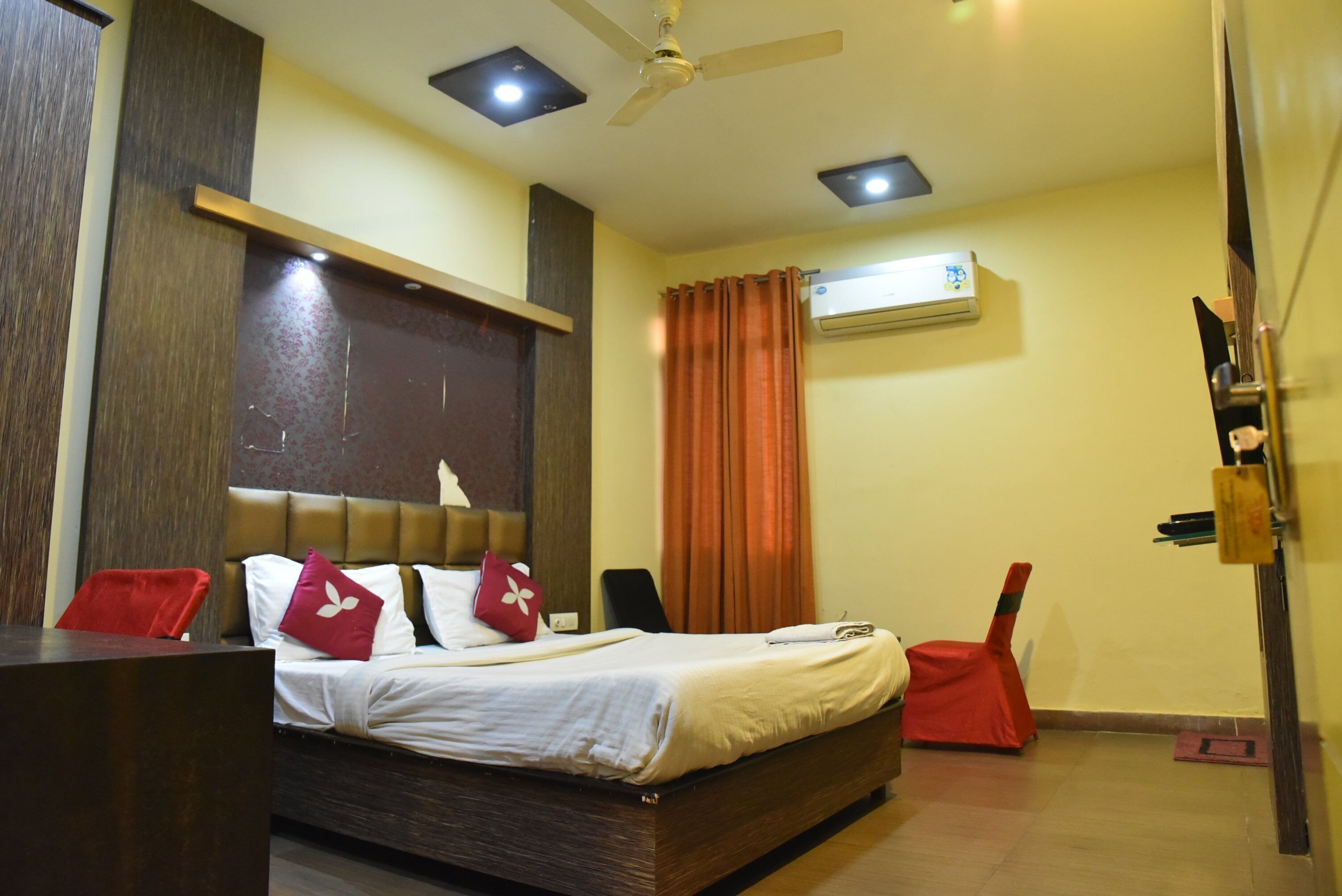 Quarto de hotel com cama, escrivaninha, cadeira, ventoinha no teto e ar condicionado.