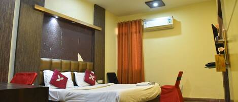 Quarto de hotel com cama, escrivaninha, cadeira, ventoinha no teto e ar condicionado.