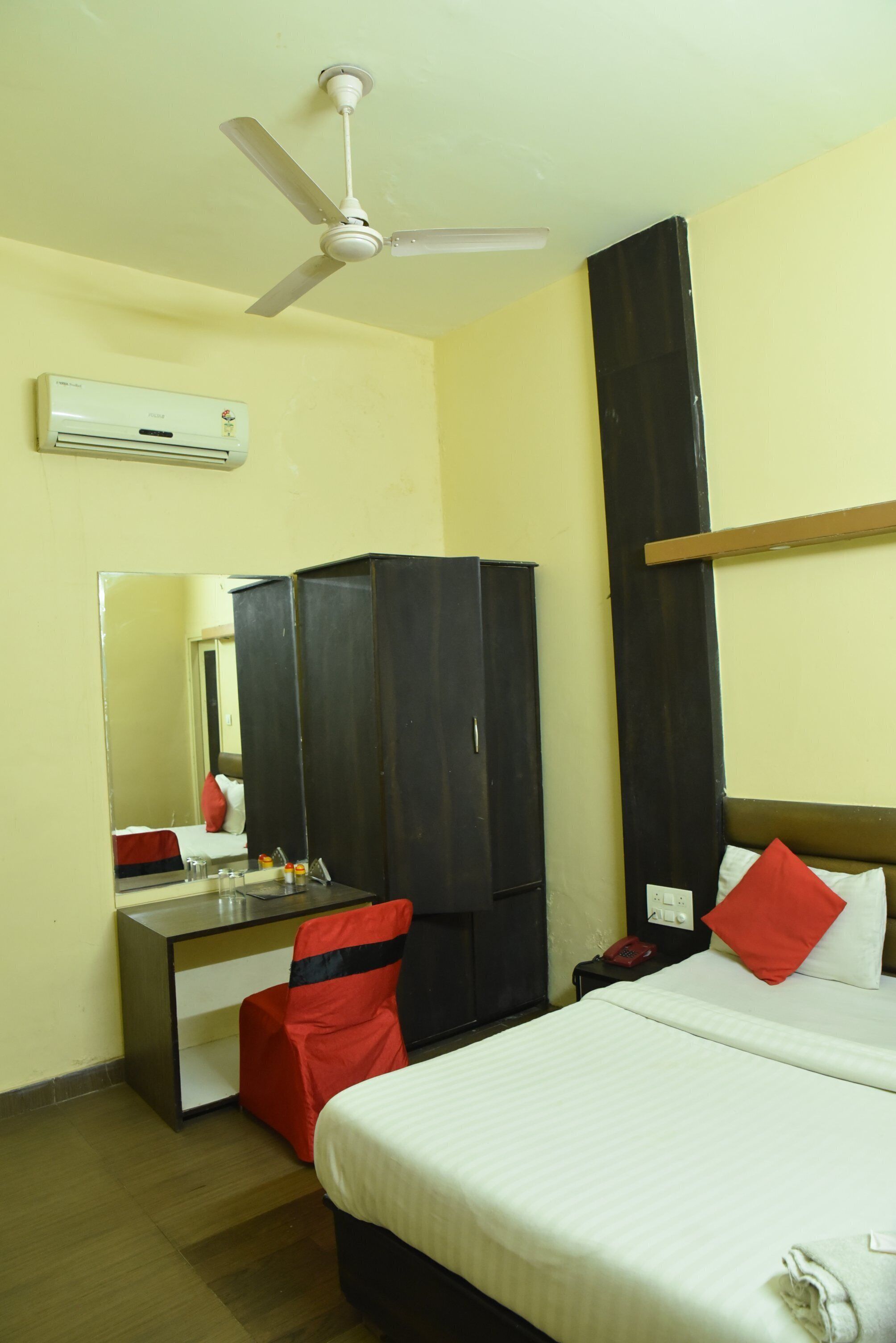 Une chambre d’hôtel équipée d’un lit, d’un bureau, d’une armoire, d’un miroir, d’un ventilateur de plafond et d’un appareil de climatisation.