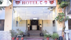 Entrada de hotel com balcão de recepção, plantas em vasos e escada que leva ao saguão.