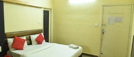 A hotel room with a bed, pillows, a folded towel, a door with a sign, and a light fixture.