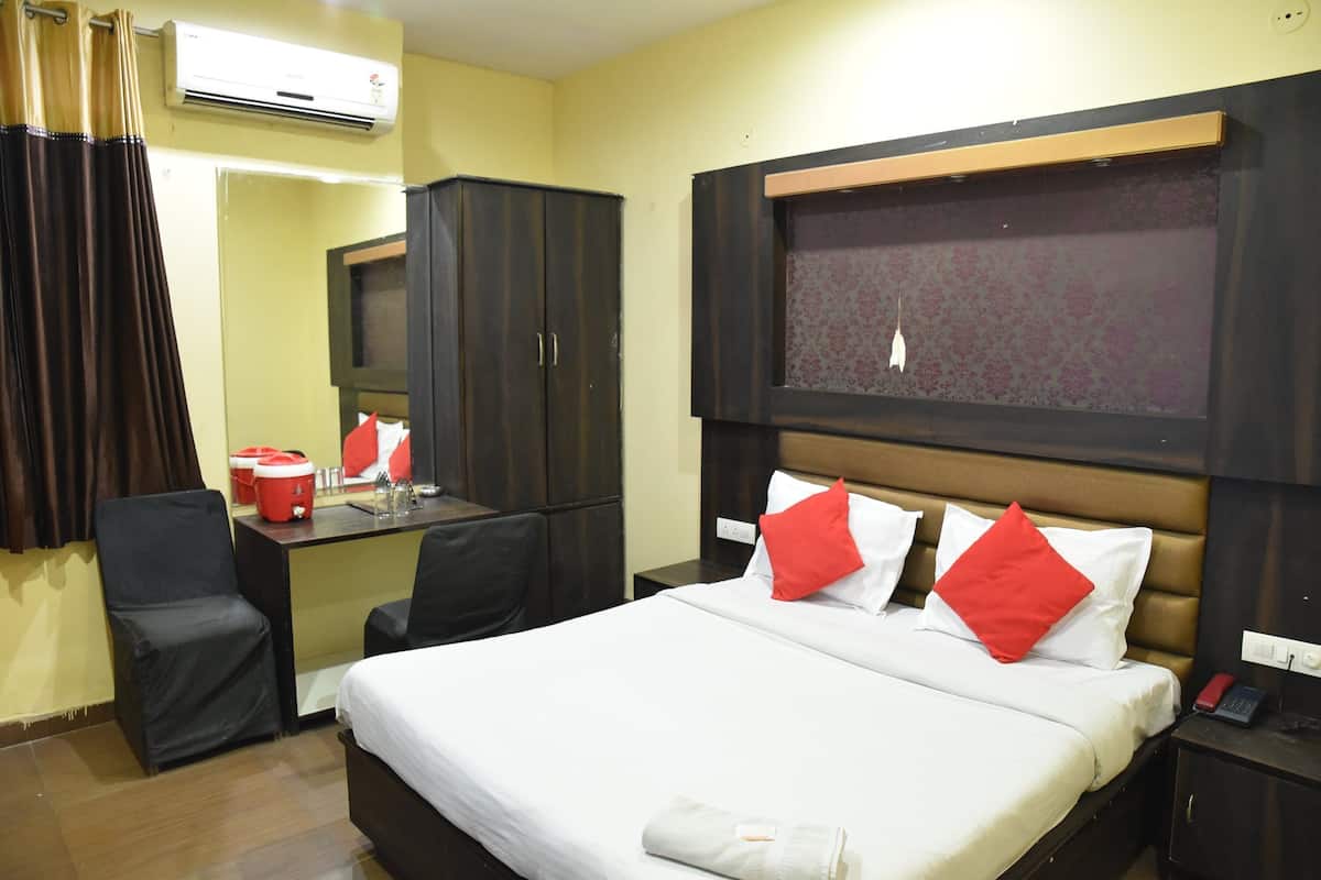A hotel room with a bed, a desk, a chair, a wardrobe, and an air conditioning unit.