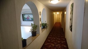 A hallway with a patterned carpet, framed pictures on the walls, and potted plants. - Landhotel Wettin (Hermsdorf-Erzgebirge)