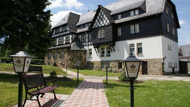 A traditional half-timbered building with a stone facade, a paved pathway, and a bench. - Landhotel Wettin (Hermsdorf-Erzgebirge)