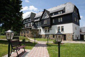 A traditional half-timbered building with a stone facade, a paved pathway, and a bench. - Landhotel Wettin (Hermsdorf-Erzgebirge)