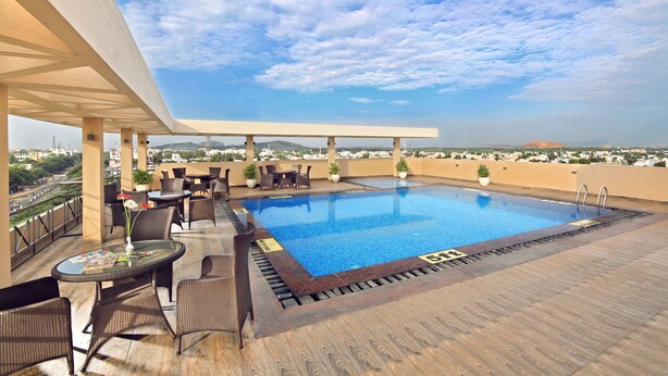 A rooftop pool with lounge chairs and tables, surrounded by a wooden deck and a clear sky. - Hotel Germanus (Madurai)