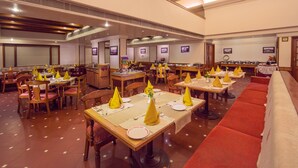 A restaurant with multiple dining tables, chairs, and a long red sofa. - Hotel Germanus (Madurai)