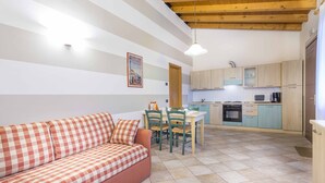 A cozy living area with a checkered sofa, a dining table with chairs, and a kitchen with light-colored cabinets and appliances. - Masorini 1, beautiful apartment near the pool.  Take a break from everyday life! (Palazzolo dello Stella)