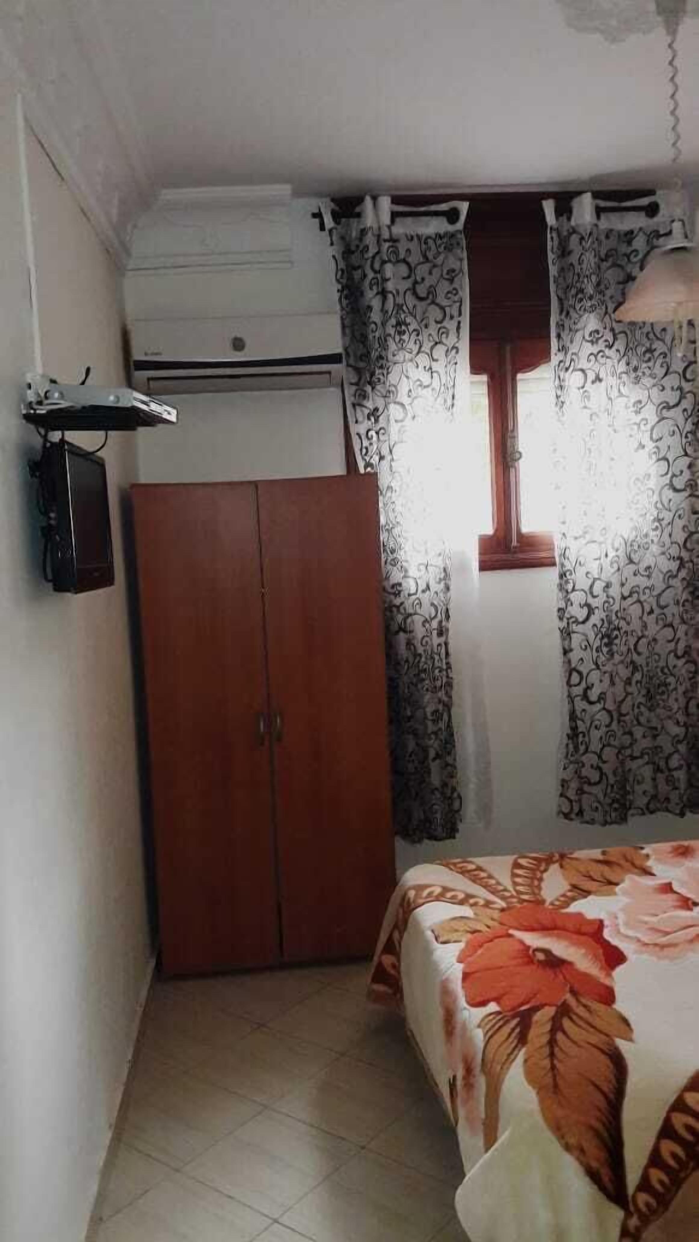 Un dormitorio con cama, armario, aire acondicionado y cortinas.