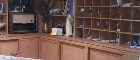Una habitación con un escritorio de madera, estanterías con diversos objetos e iluminación fluorescente en el techo.