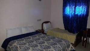 Una habitación con dos camas, una mesita de noche, una lámpara y una cortina.