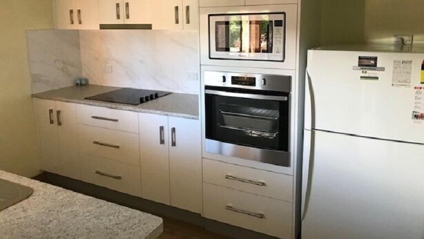 A kitchen with white cabinets, a built-in oven, and a refrigerator. - Akuna 8 (Forster)