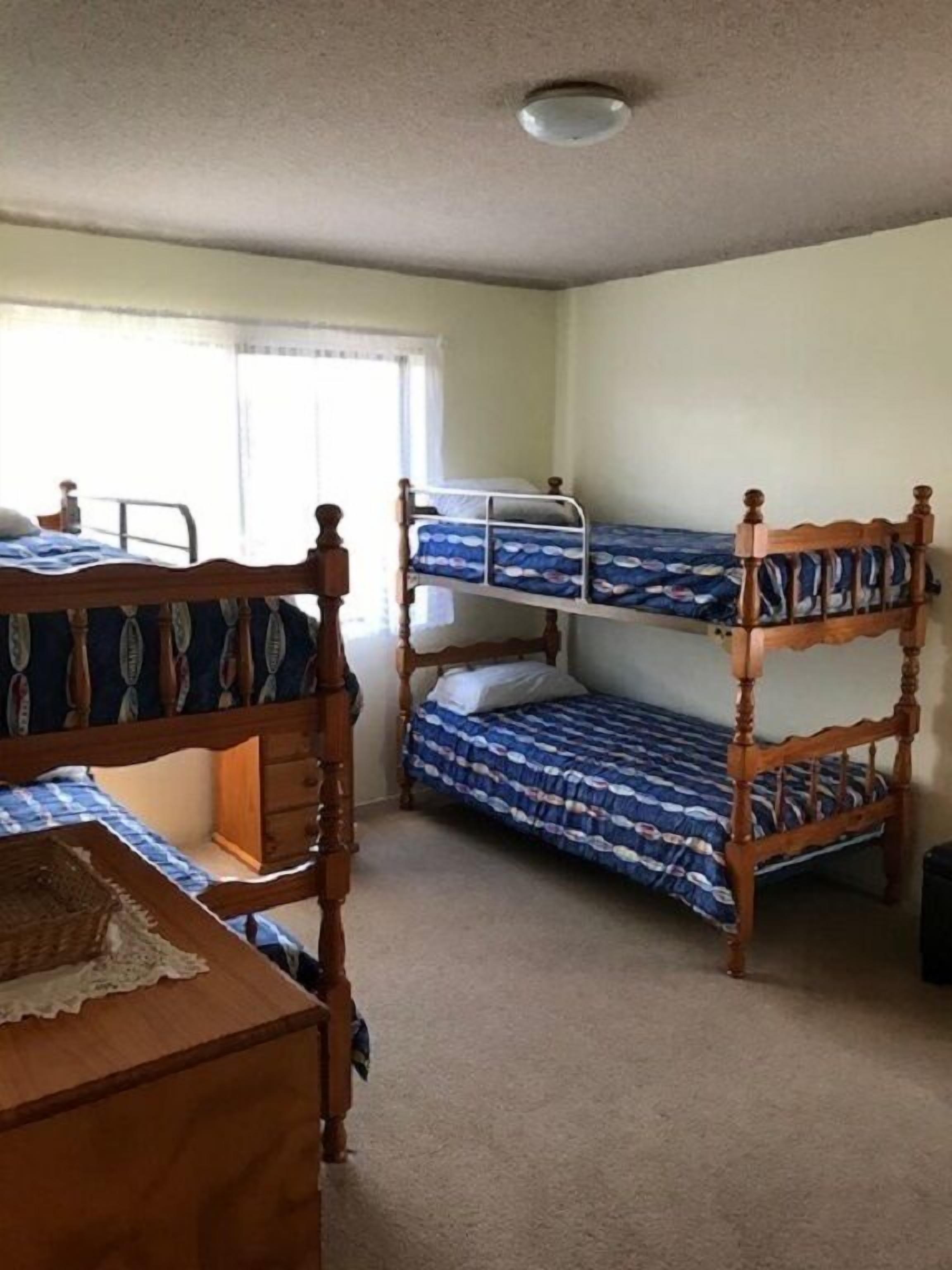 A room with three wooden bunk beds, a wooden dresser, and a window with curtains.