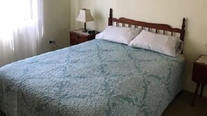 A bedroom with a bed, a ceiling fan, a nightstand with a lamp, and a painting on the wall. - Akuna 8 (Forster)