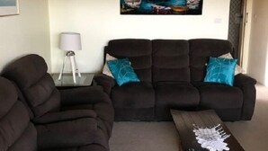 A living room with two dark brown sofas, a wooden coffee table, and a painting of a harbor scene on the wall. - Akuna 8 (Forster)
