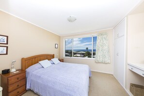 Un dormitorio con cama, mesita de noche, cómoda, ventana con vistas y luz de techo.