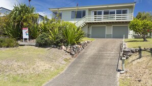 A two-story house with a front porch, a driveway, and a signboard. - Beach Cottage (Forster)