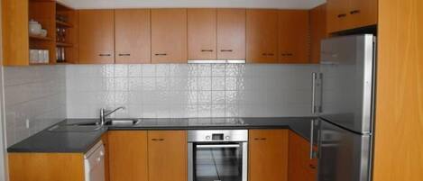A kitchen with wooden cabinets, a stainless steel refrigerator, and a built-in oven.