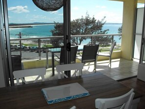 A balcony with a view of the ocean, a table with chairs, and a hanging light fixture.