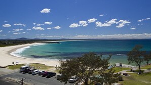 Une vue sur la plage, avec un ciel dégagé, un espace de stationnement et une côte visible au loin.