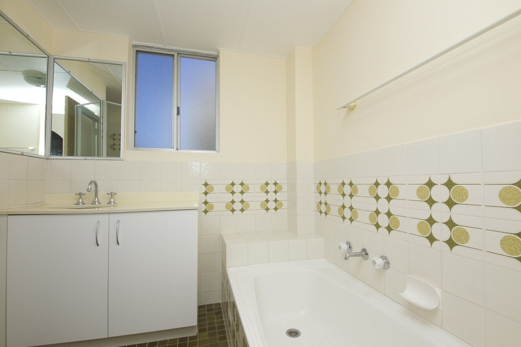 Een badkamer met een wit wastafel, een spiegel, een raam en een bad.