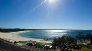 Ein Strand mit blauem Himmel und einem Parkplatz mit Fahrzeugen.