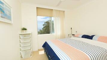 A bedroom with a bed, a window with curtains, a desk, and a plant.