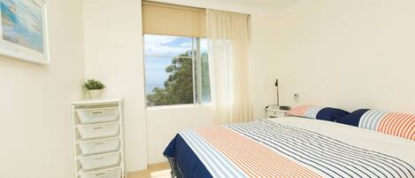 A bedroom with a bed, a window with curtains, a desk, and a plant.