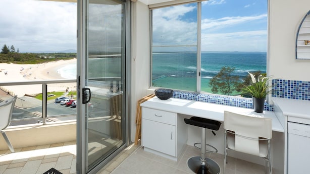 A balcony with a glass door leading to a beach view, a white countertop, and a chair. - Beachpoint Unit 501 (Forster)