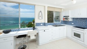 A modern kitchen with a view of the ocean, white cabinets, a microwave, and a dishwasher. - Beachpoint Unit 501 (Forster)