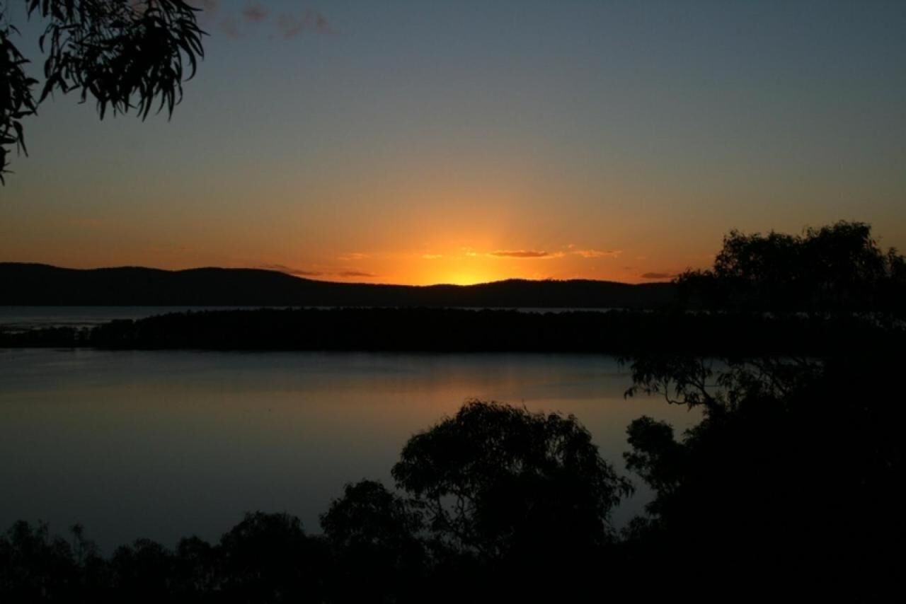 A sunset over a calm lake with silhouettes of trees and hills in the background.