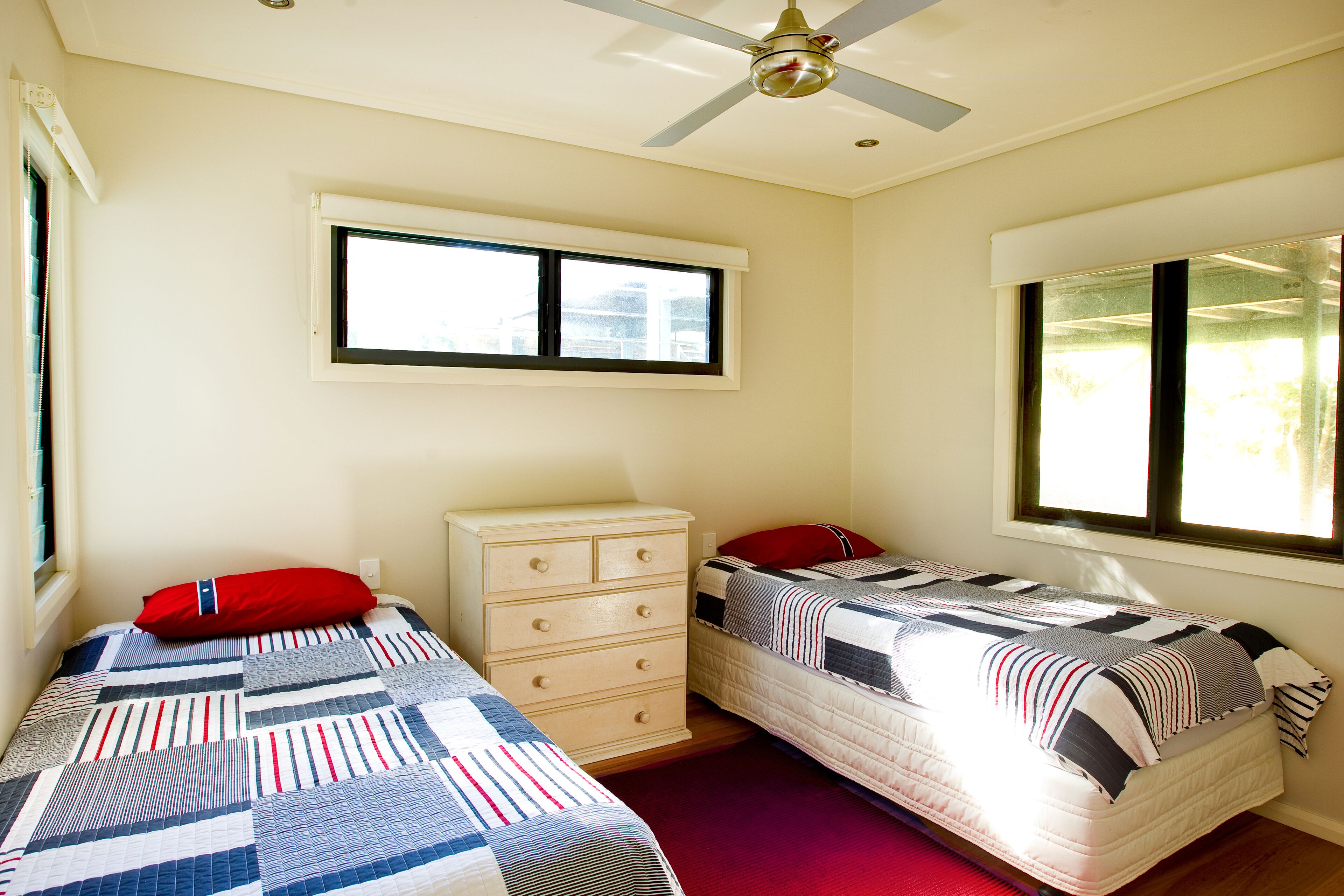 A bedroom with two beds, a dresser, a ceiling fan, and windows.