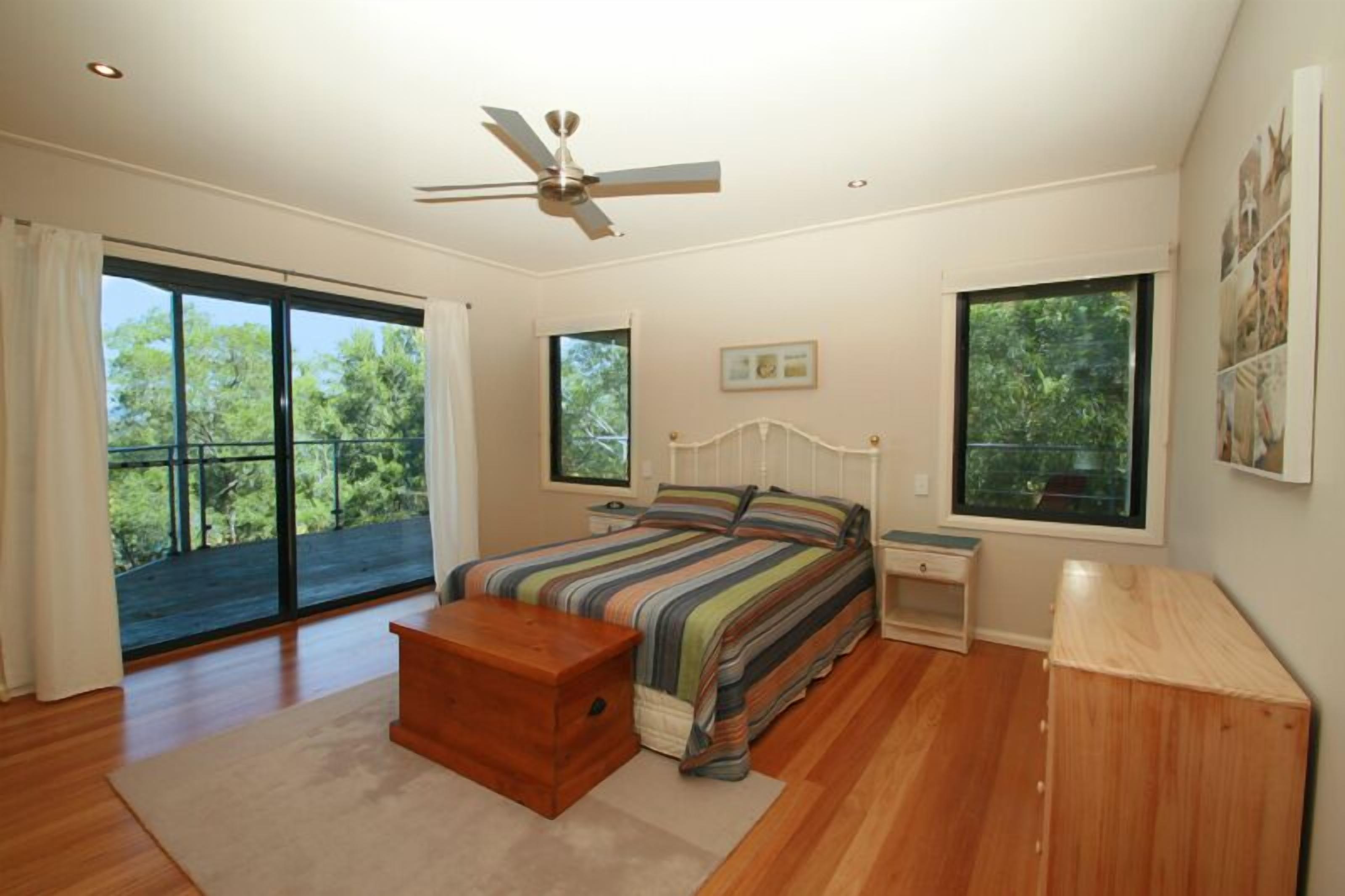 A bedroom with a large bed, a nightstand, a wooden bench, and a ceiling fan.