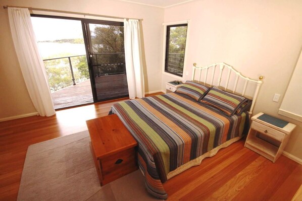 A bedroom with a bed, a nightstand, a wooden bench, and a sliding glass door leading to an outdoor area. - Berringar (Green Point)