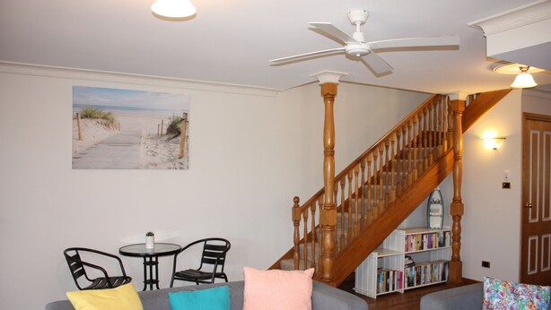 A living room with a gray sofa, a wooden staircase, and a bookshelf. - Birchgrove Terrace Unit 6 (Tuncurry)