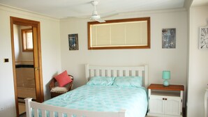 A bedroom with a bed, a nightstand, a chair, a window with blinds, and a ceiling fan. - Birchgrove Terrace Unit 6 (Tuncurry)