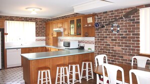 A kitchen with wooden cabinets, a built-in microwave, and a brick wall. - Birchgrove Terrace Unit 6 (Tuncurry)
