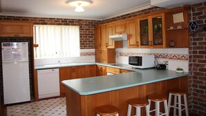 A kitchen with wooden cabinets, a built-in microwave, and a window with blinds. - Birchgrove Terrace Unit 6 (Tuncurry)