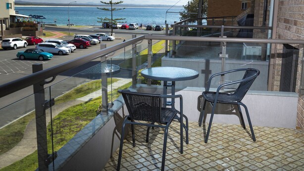 A balcony with a glass railing, two chairs, and a small table. - Breakers 3 (Forster)