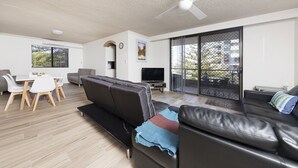 A modern living room with a flat-screen TV, a ceiling fan, and a dining area with a table and chairs. - Breakers 3 (Forster)
