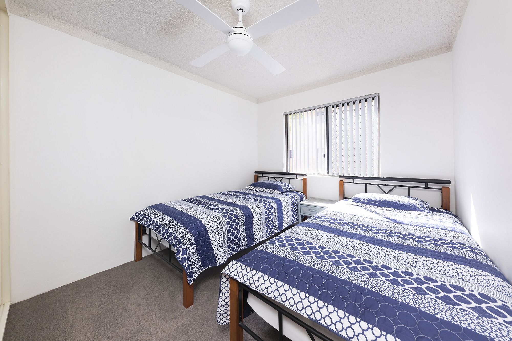 Un dormitorio con dos camas individuales, un ventilador de techo y una ventana con persianas.