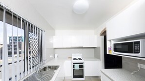 A compact kitchen with white cabinets, a built-in microwave, a stove, and a sink. - Breakers 3 (Forster)