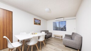A modern living room with a dining table, white chairs, a grey sofa, and a small side table. - Breakers 3 (Forster)