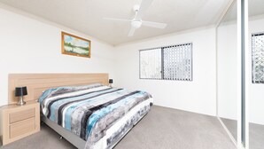 A bedroom with a bed, a nightstand, a ceiling fan, a window with bars, and a painting on the wall. - Breakers 3 (Forster)