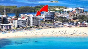 A coastal cityscape with a beach, high-rise buildings, and a red arrow pointing to a specific building. - Ebbtide Unit 04 (Forster)