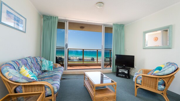 A balcony with a view of the ocean, furnished with wicker chairs and a sofa, and a flat-screen TV. - Ebbtide Unit 07 (Forster)