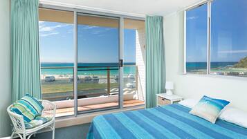 Quarto de hotel com uma grande porta de vidro deslizante que dá para uma varanda com vista para a praia e o oceano.