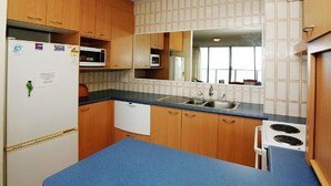 A compact kitchen with wooden cabinets, a white refrigerator, a microwave, a sink, and a stove. - Ebbtide Unit 33 (Forster)
